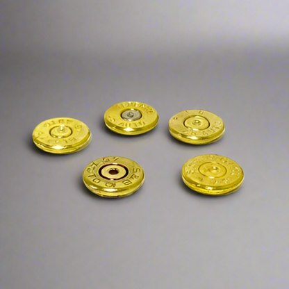 Five gold brass casing slices spread out on a gray background, one showing a silver primer center.