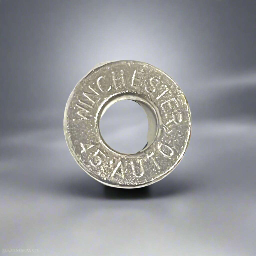 A macro view of a single deprimed Winchester 45 Auto nickel pistol shell slice against a gradient grey background.