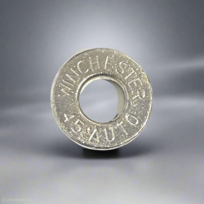 A macro view of a single deprimed Winchester 45 Auto nickel pistol shell slice against a gradient grey background.