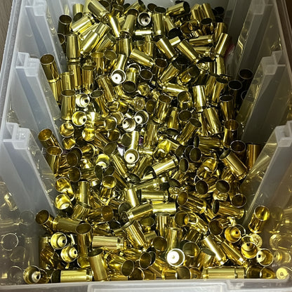 Hundreds of gold 45 ACP brass casings piled inside a white plastic storage bin, mixed mouths and rims facing up.