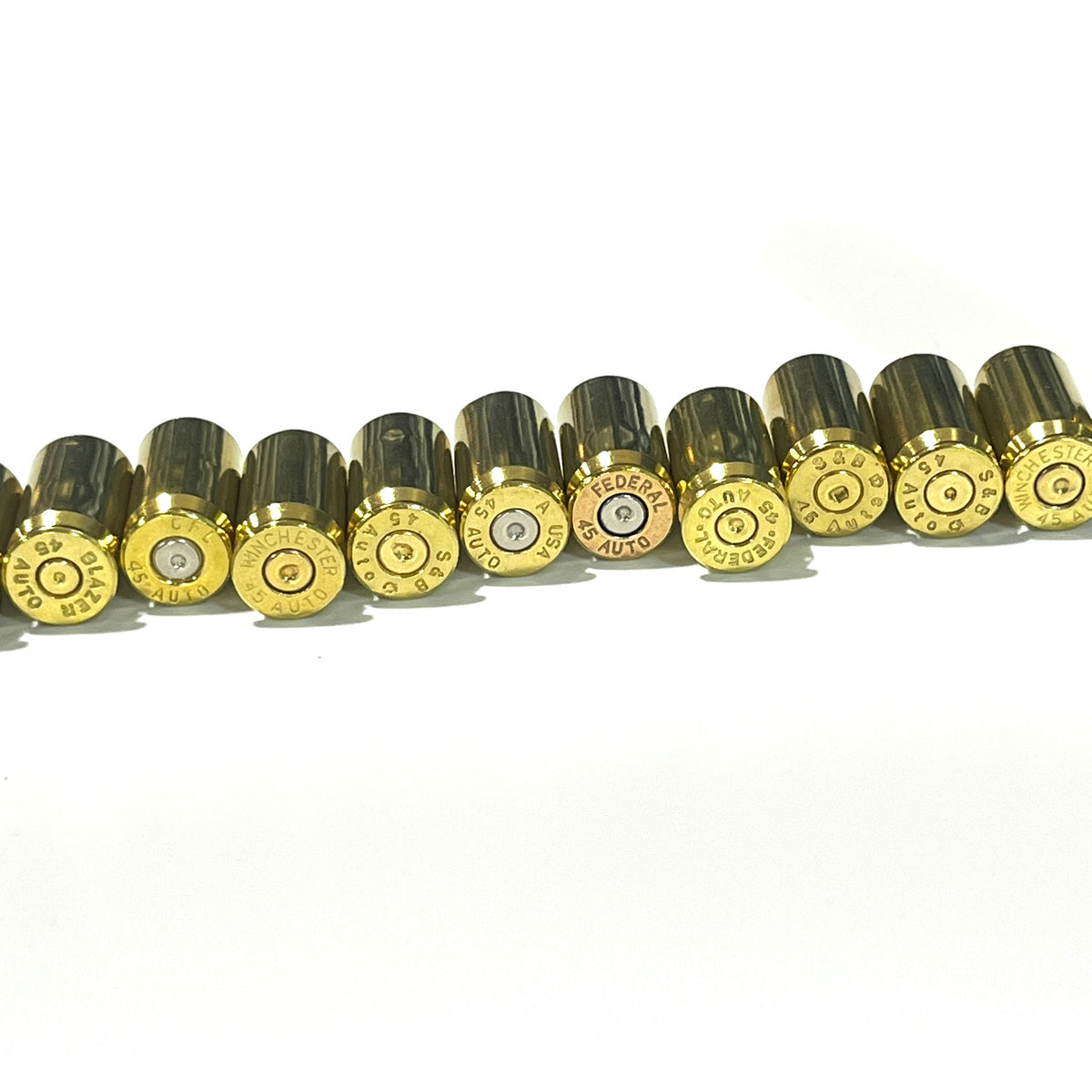 A row of gold 45 ACP brass on their sides, showing mixed headstamps spent primers including Winchester, Federal, and S&B.