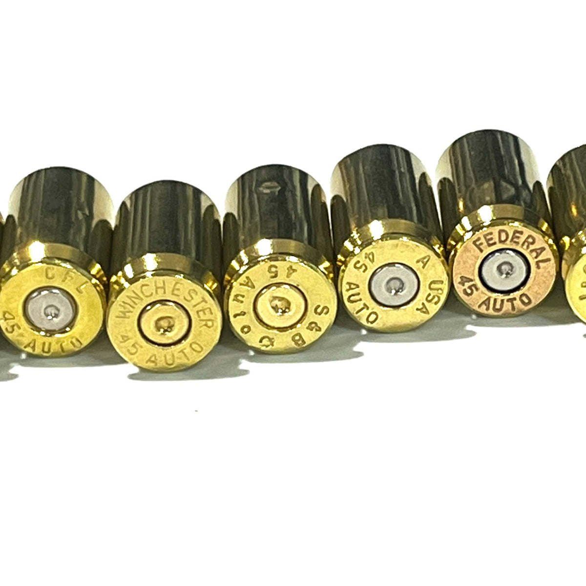 Close-up of gold 45 ACP brass shells in a row, headstamps clearly visible spent primers: CFL, Winchester, S&B, USA, Federal.