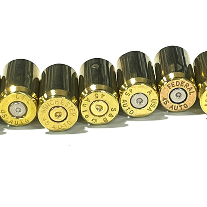 Close-up of gold 45 ACP brass shells in a row, headstamps clearly visible spent primers: CFL, Winchester, S&B, USA, Federal.