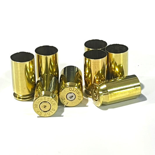Seven gold 45 ACP brass spent casings, some upright with open case mouths, others tipped over showing Winchester and F.C headstamps with spent primers.