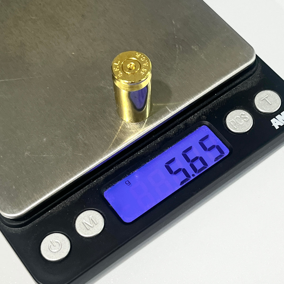 A single gold 45 ACP spent brass shell standing on a digital scale, display reading 5.65 grams.