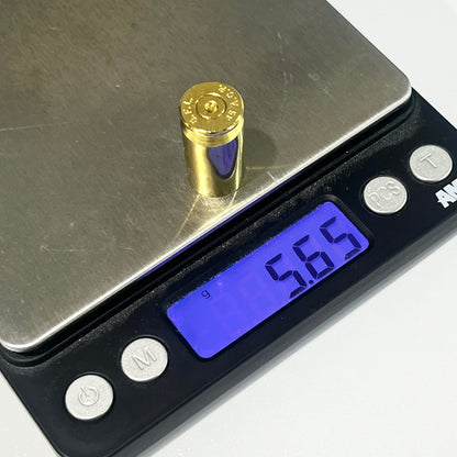 A single gold 45 ACP spent brass shell standing on a digital scale, display reading 5.65 grams.