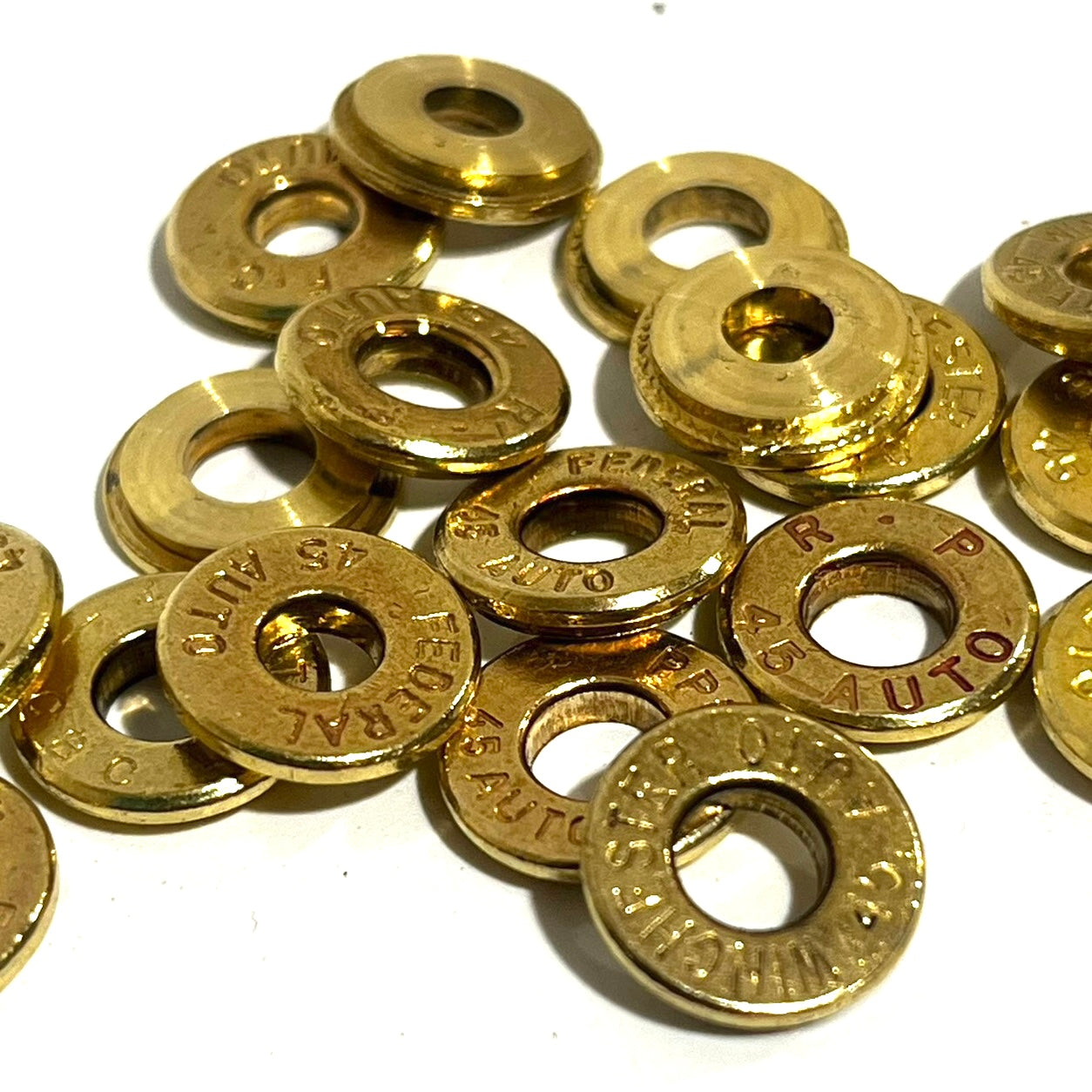 Pile of gold brass deprimed 45 Auto bullet slices with Federal and R-P headstamps on a white background