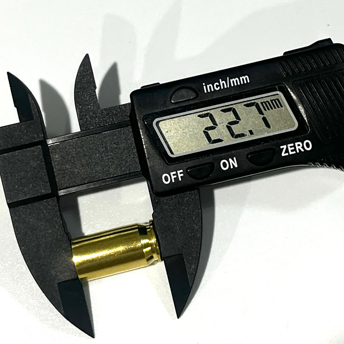 A gold 45 ACP brass casing held in a digital caliper's jaws, display reading 22.7 mm case length.