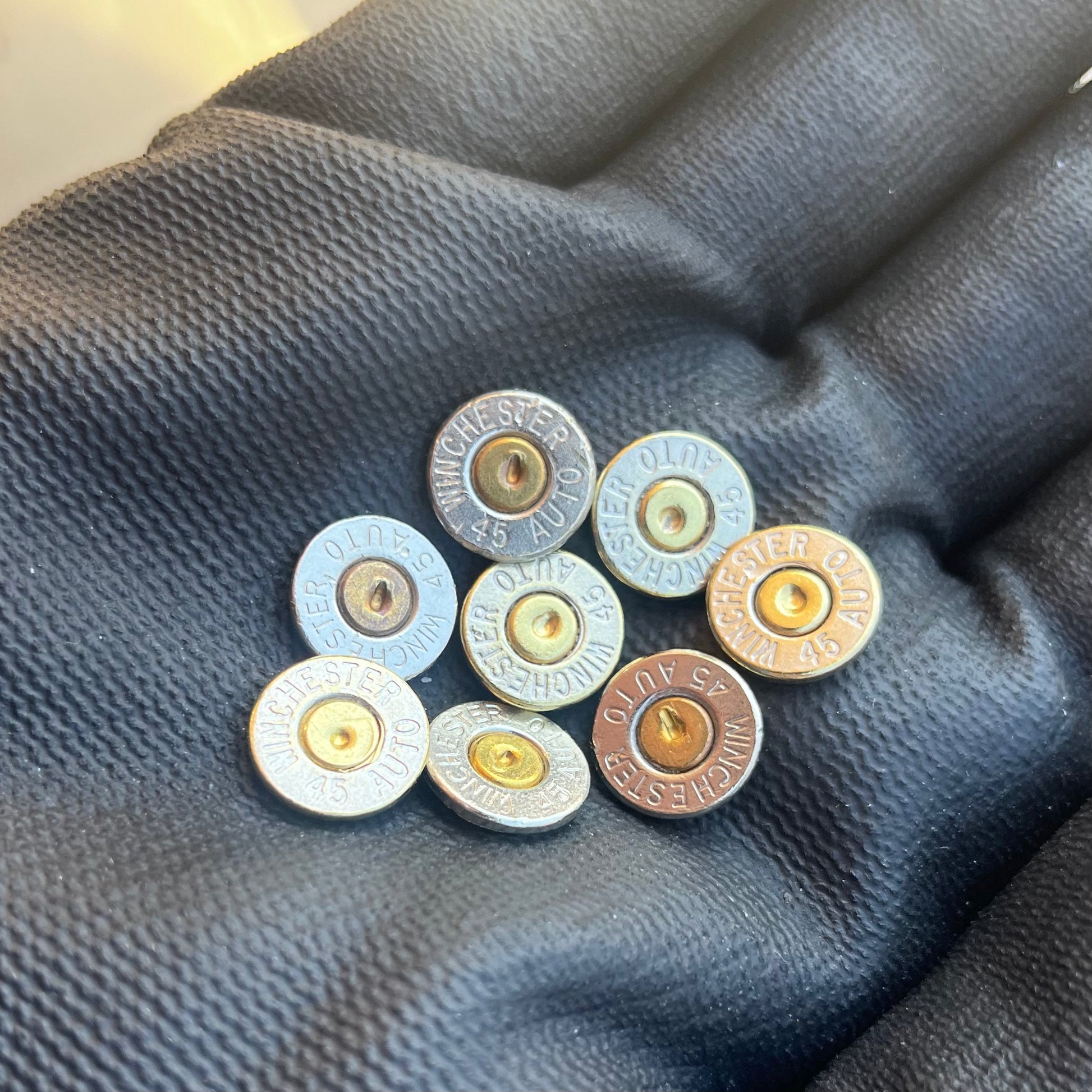 8 nickel 45 ACP bullet slices with gold and copper primers, engraved Winchester 45 Auto headstamps, held in a gloved hand