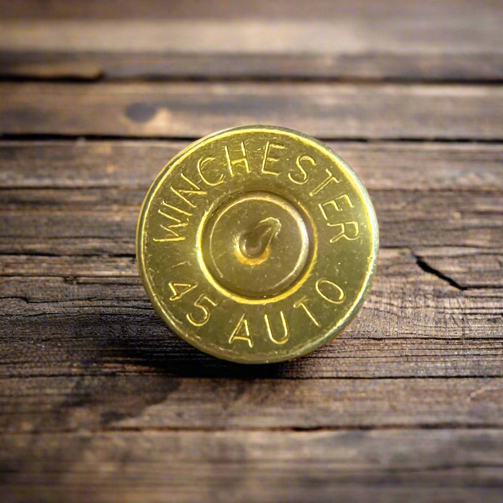Close-up of a gold 45 ACP Winchester brass bullet slice with a drilled hole, on a wood surface