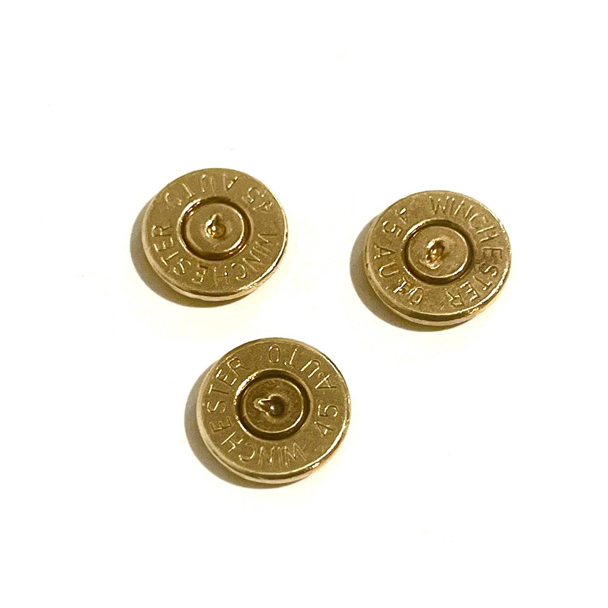 3 gold 45 ACP brass bullet slices with Winchester headstamps on a white background