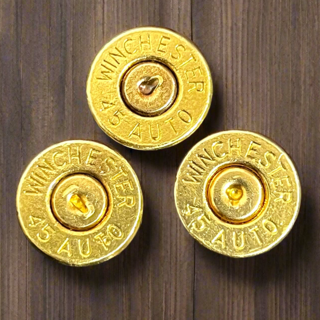 3 gold 45 ACP brass bullet slices with Winchester headstamps on a wood surface