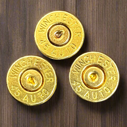 3 gold 45 ACP brass bullet slices with Winchester headstamps on a wood surface