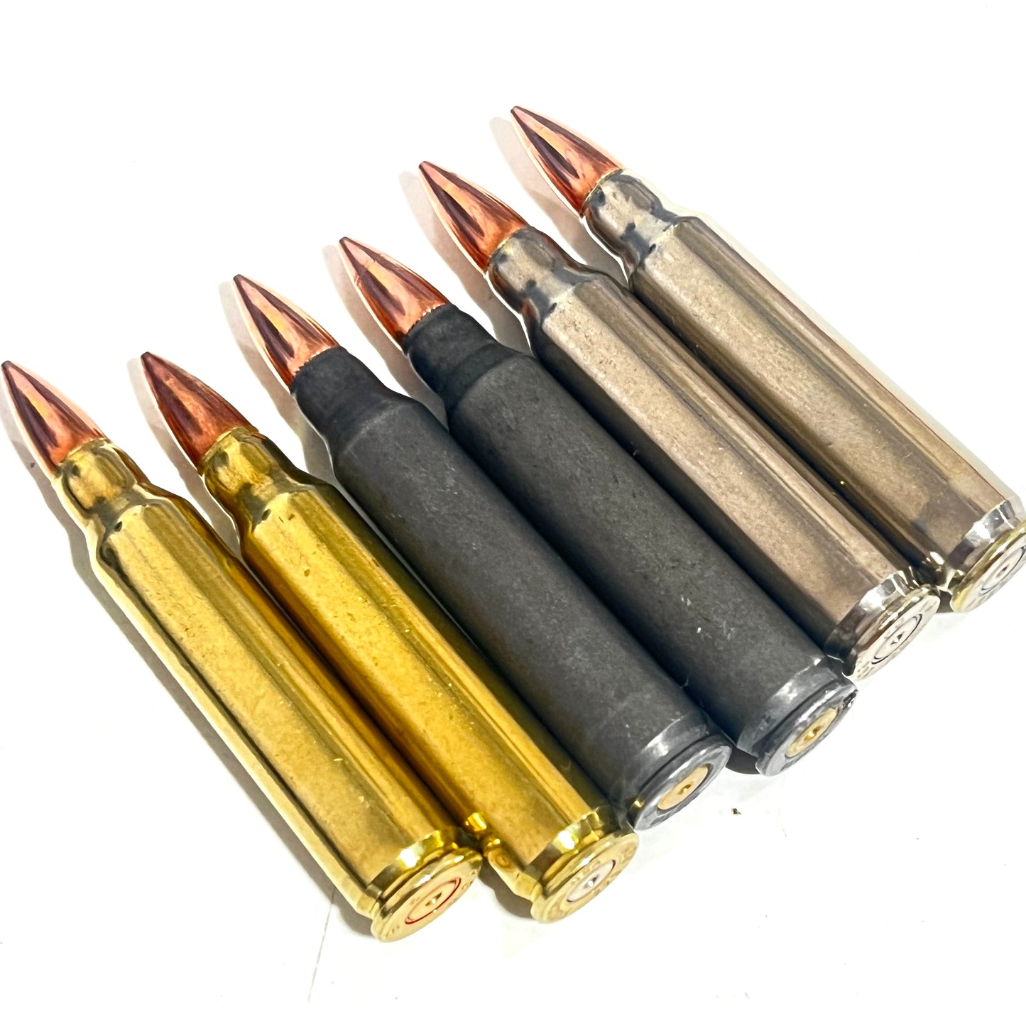 Six .223/5.56 casings in black, brass, and silver finishes lie diagonally, showing their base rims.