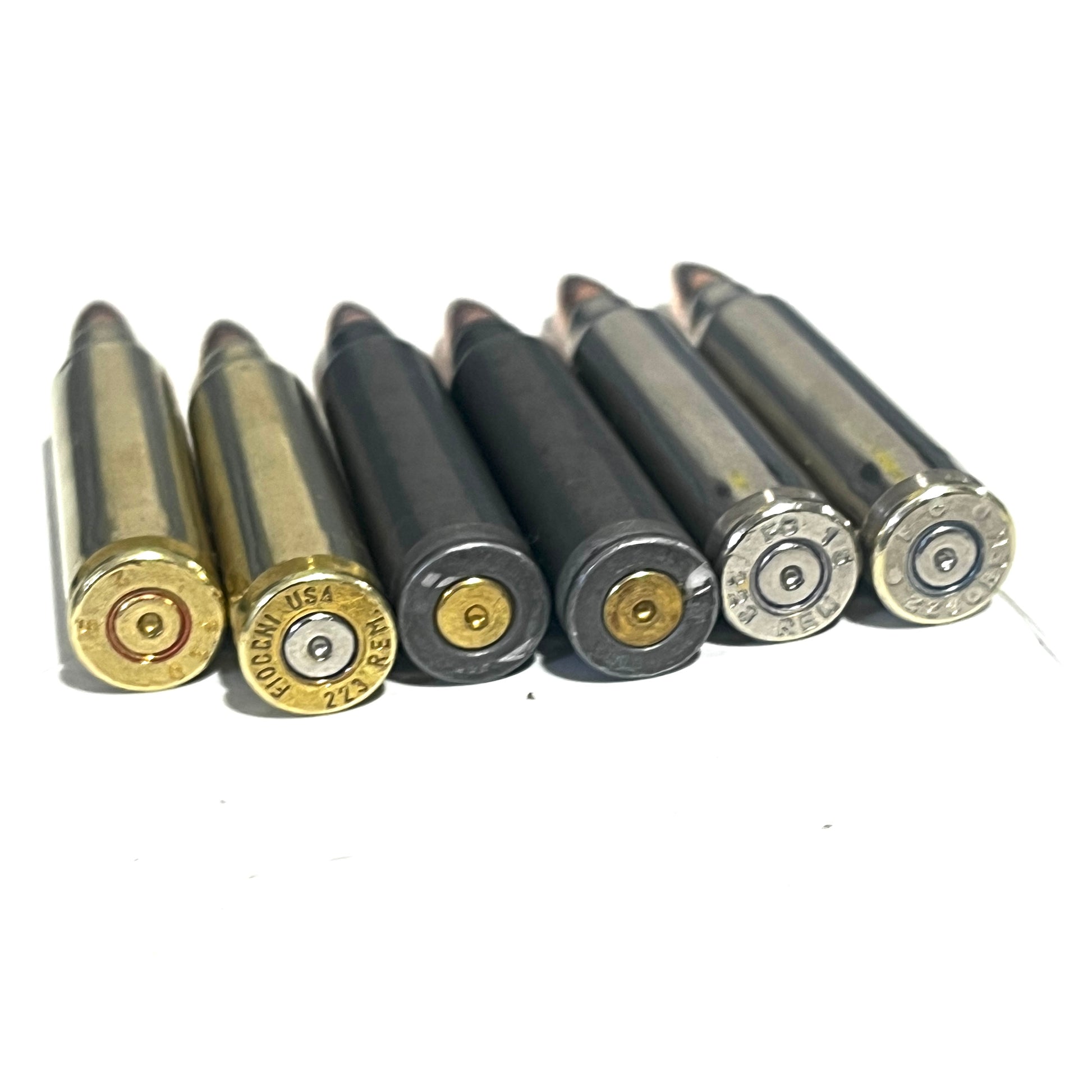 Six .223/5.56 shells in brass, black, and silver finishes lie side by side, showing visible headstamps.