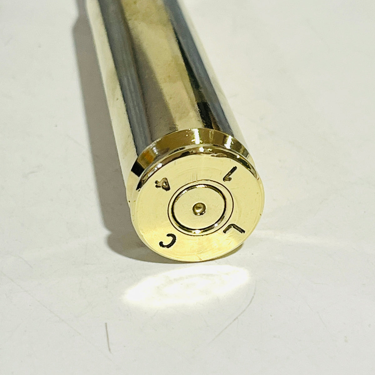 Base of a mirror-polished .50 BMG brass shell stamped LC, showing a dimpled spent primer, on a white surface