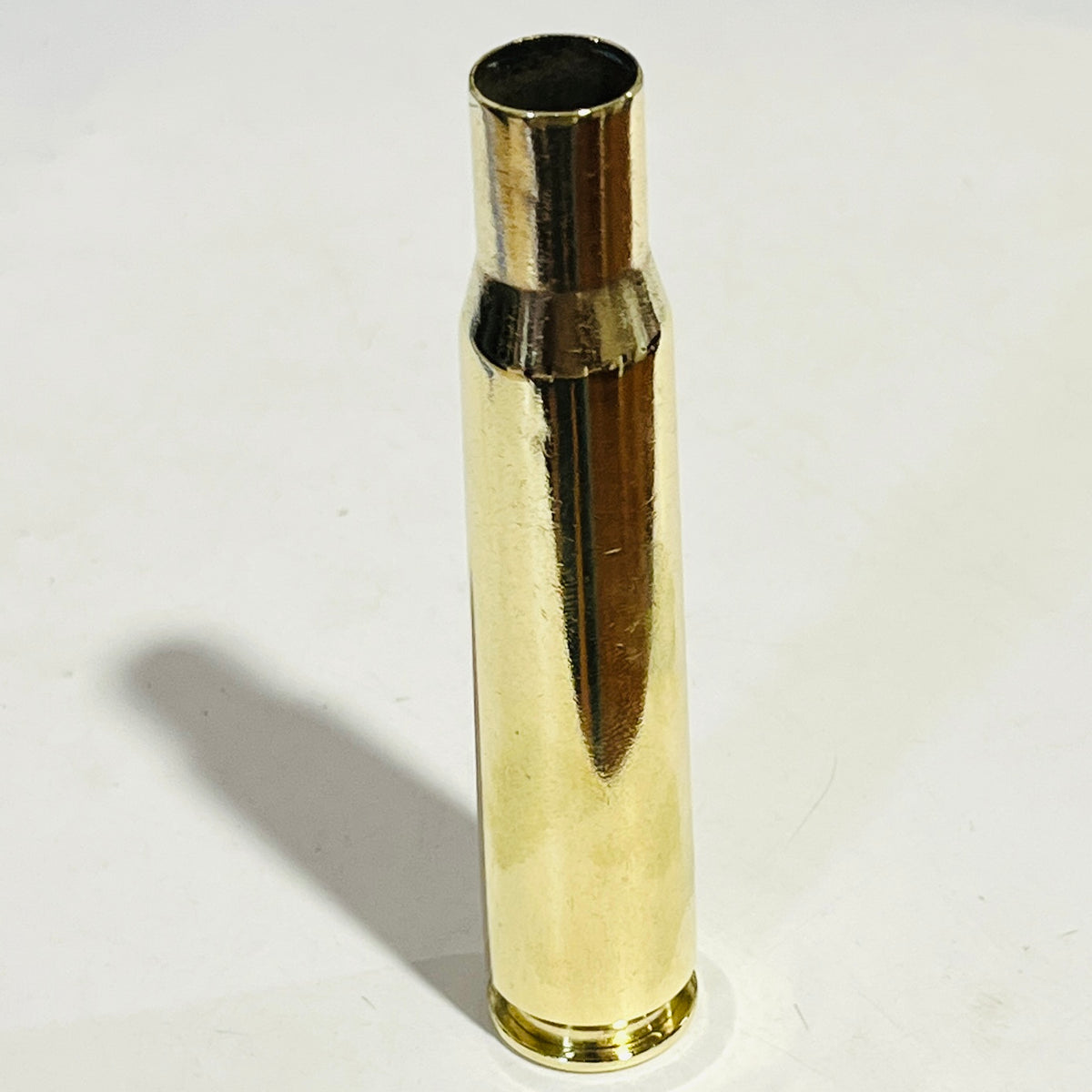 Hand-polished .50 BMG brass casing standing upright on a white surface, casting a soft shadow
