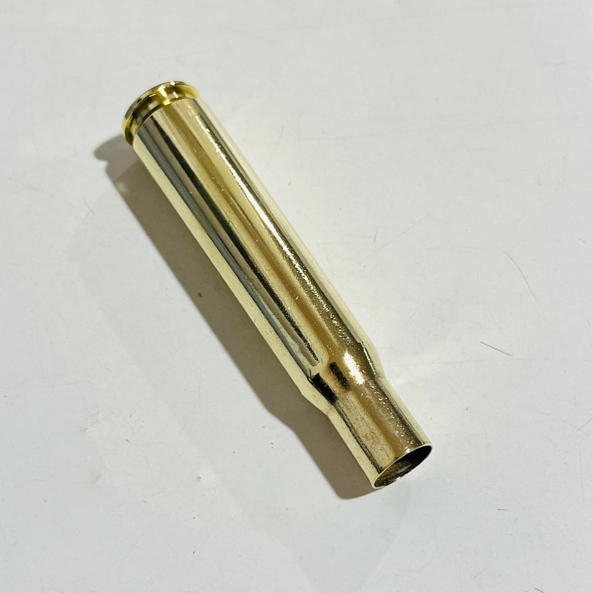 Polished .50 BMG brass cartridge case lying diagonally on a white surface, open mouth toward the camera