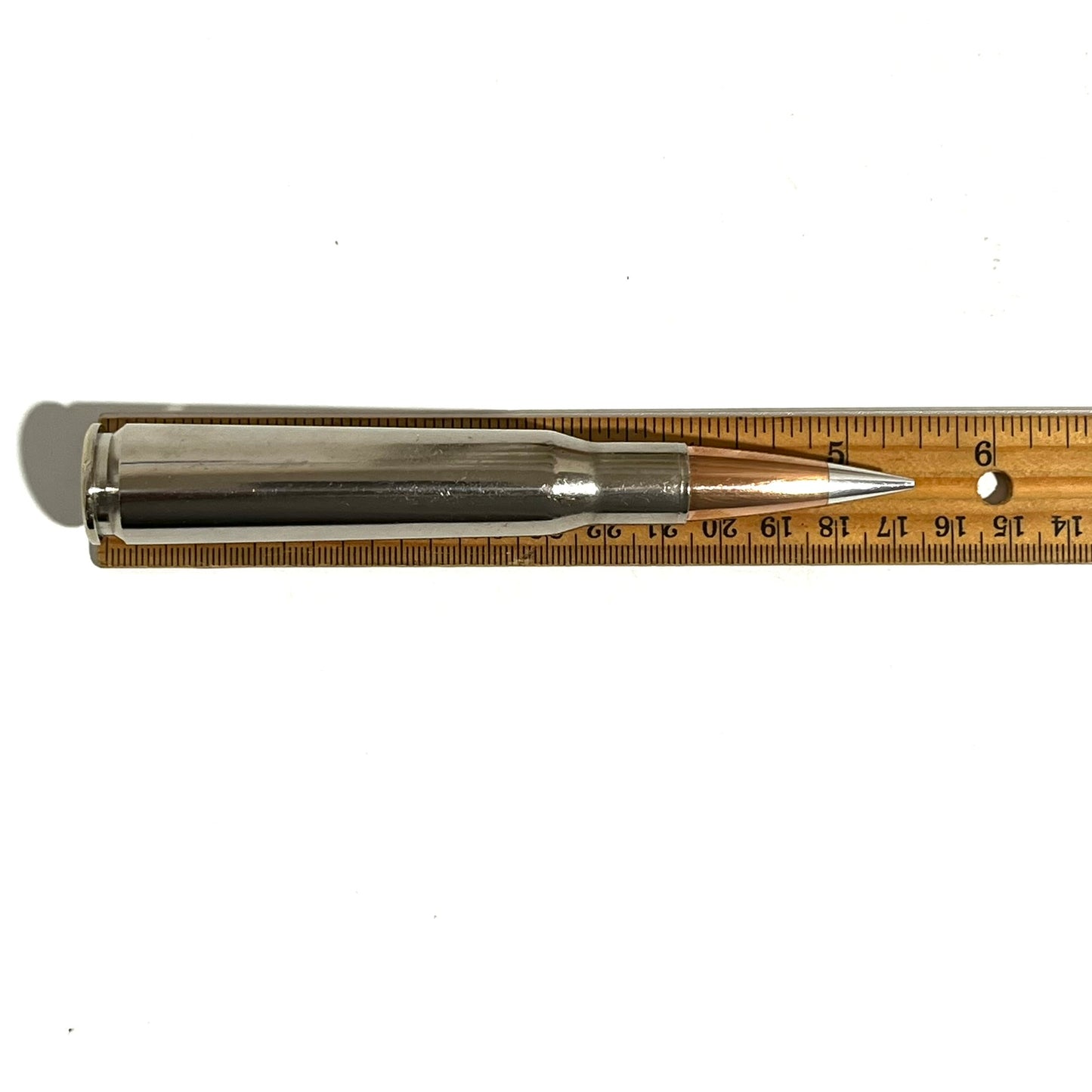 Polished silver nickel 50 cal BMG dummy round measurement showing 5.5 inch length next to a wooden ruler.
