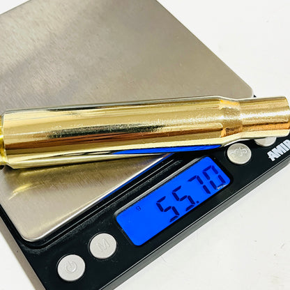 Once-fired .50 BMG polished brass shell lying across a digital scale reading 55.70 grams