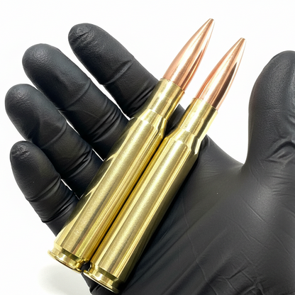 Two brass 50 cal dummy weighted rounds with copper bullets held in a hand wearing a black glove against a white background.
