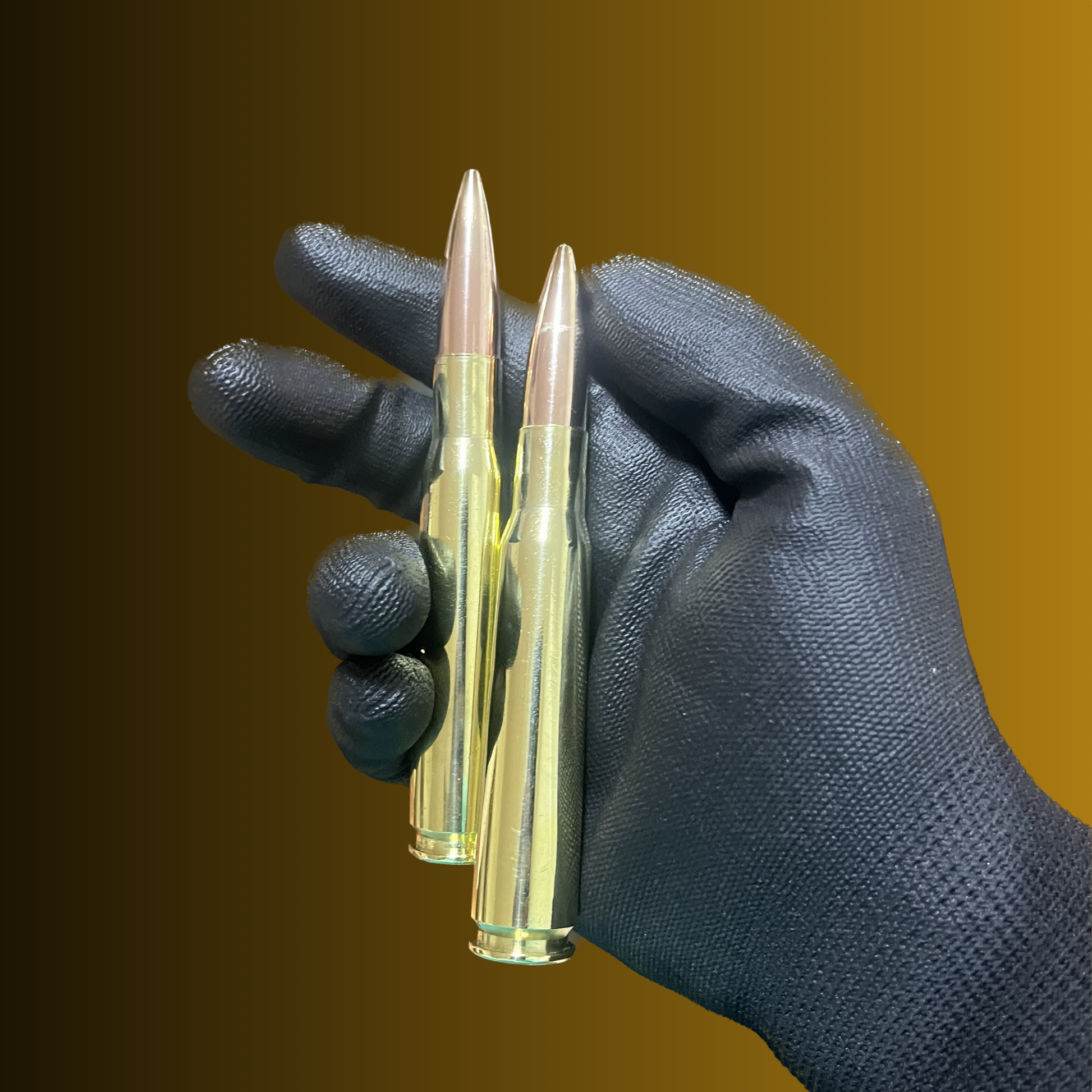 Two polished brass rounds with copper tips held upright in a black gloved hand against a brown background.
