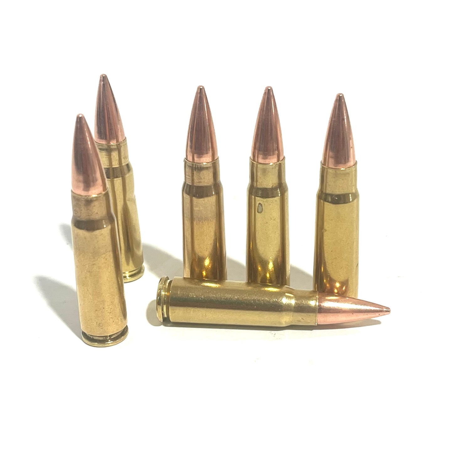 Five standing and one laying 7.62x39 dummy rounds with authentic brass wear and copper bullet profiles on white.
