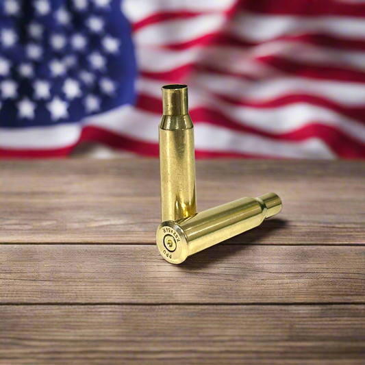 Two polished 7.62x54R empty brass casings on wood; one lying showing PPU headstamp. American flag background.
