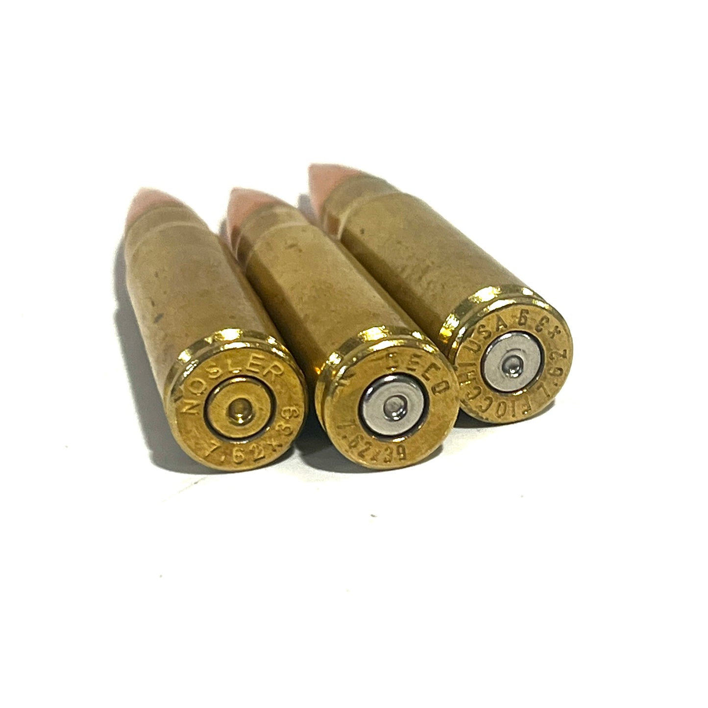 3 brass 7.62x39 dummy rounds with red-tipped bullets lying at an angle on a white background
