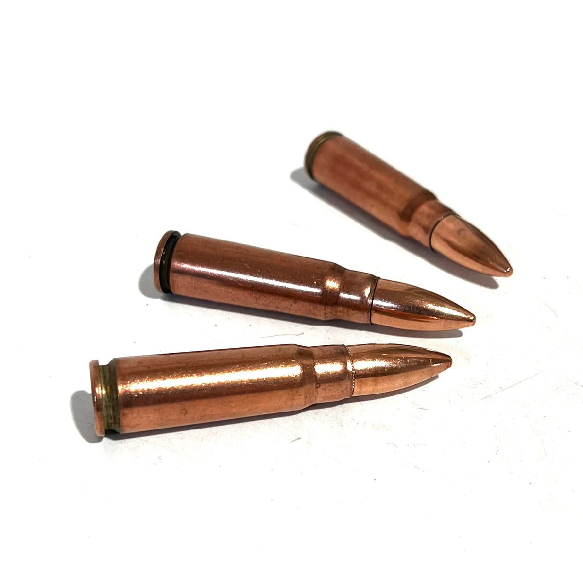 3 copper 7.62x39 dummy rounds lying on a white background at an angle