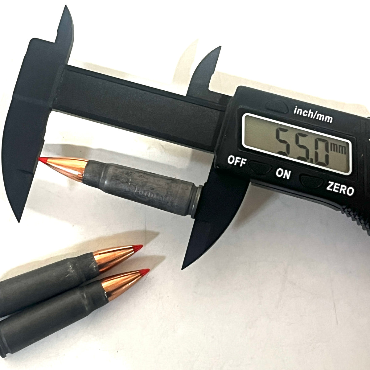 Digital caliper measuring a steel 7.62x39 dummy round's length at 55.0 millimeters, with two more rounds beside it