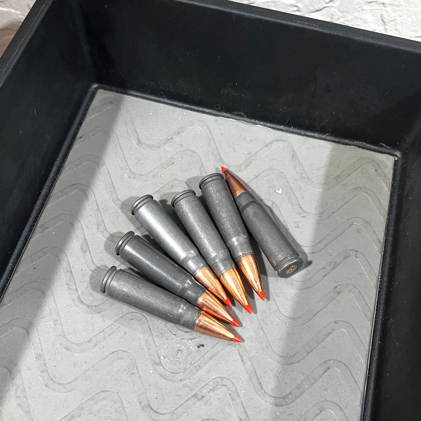 7 steel 7.62x39 dummy rounds with red-tipped bullets scattered in a black tray