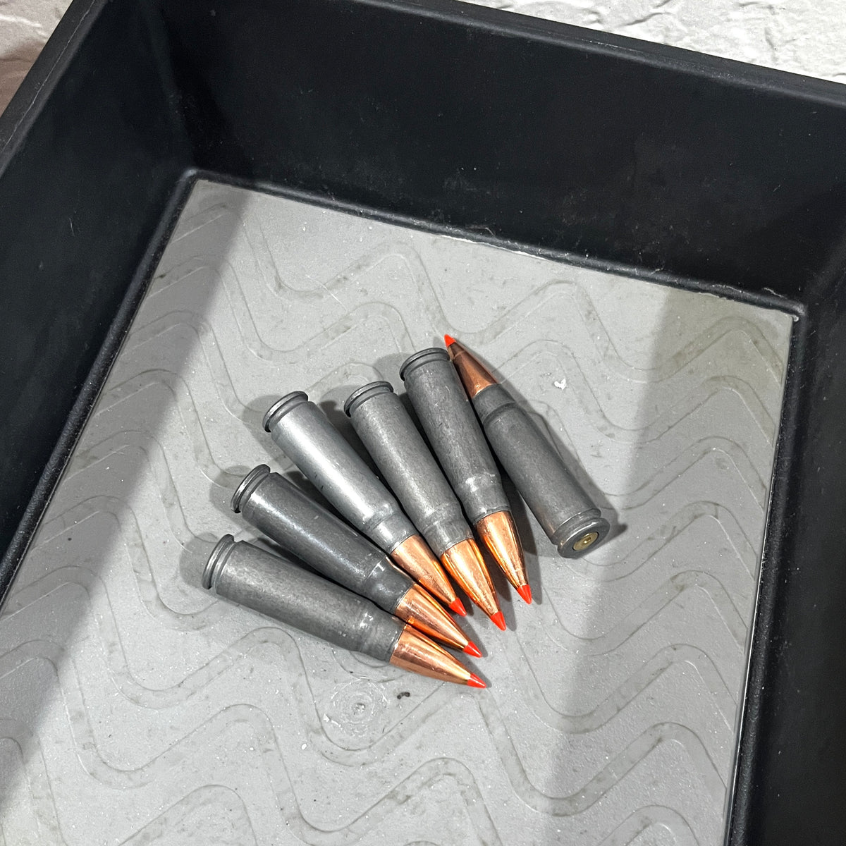 7 steel 7.62x39 dummy rounds with red-tipped bullets scattered in a black tray