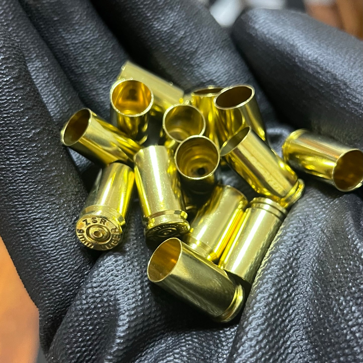 Gloved hand holding polished 9mm brass shells with spent primer dimples and open mouths visible.
