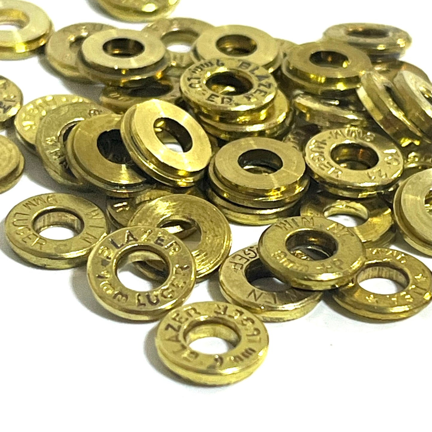 A macro view of 9mm deprimed brass slices in a pile, showing mixed headstamp markings from multiple sources.