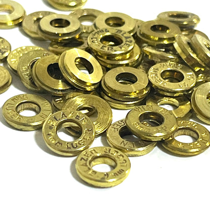 A macro view of 9mm deprimed brass slices in a pile, showing mixed headstamp markings from multiple sources.