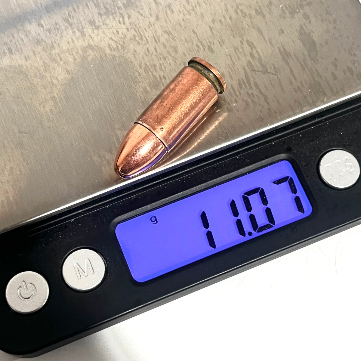 Copper 9mm Luger dummy round on a digital scale reading 11.07 grams