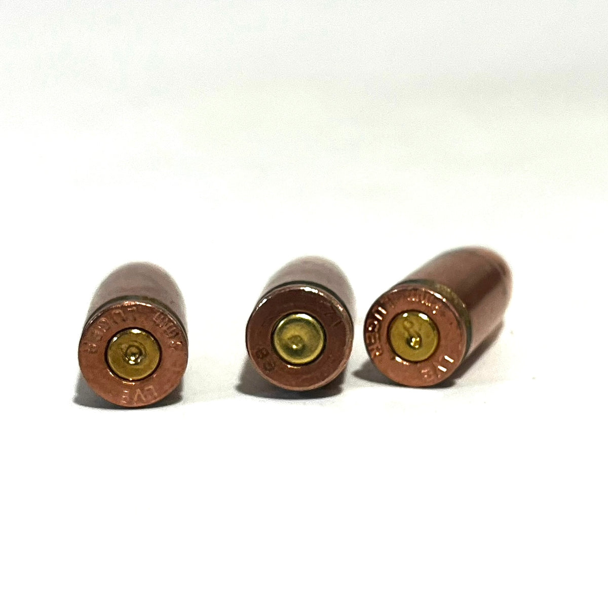 3 copper 9mm Luger dummy rounds viewed from the base showing brass primers and headstamps