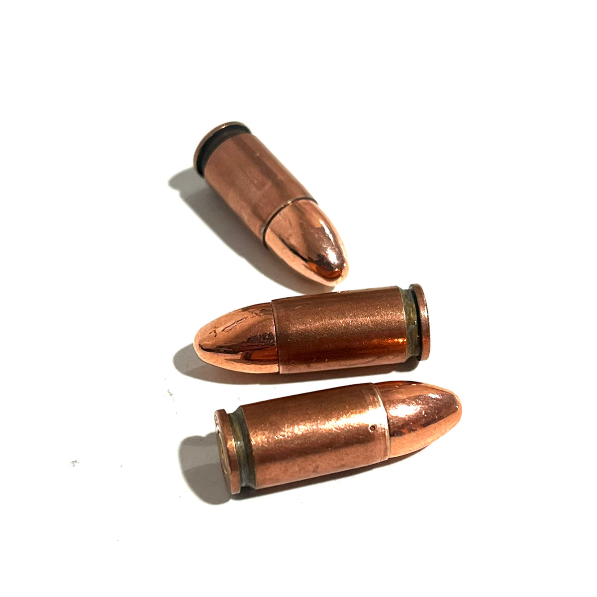 3 copper 9mm Luger dummy rounds lying at different angles on a white background