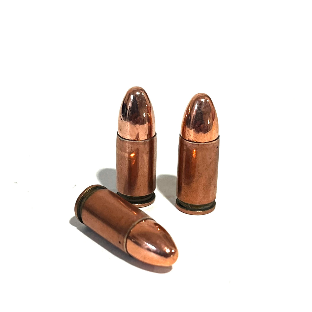 3 copper 9mm Luger dummy rounds, two standing and one lying diagonally, on a white background