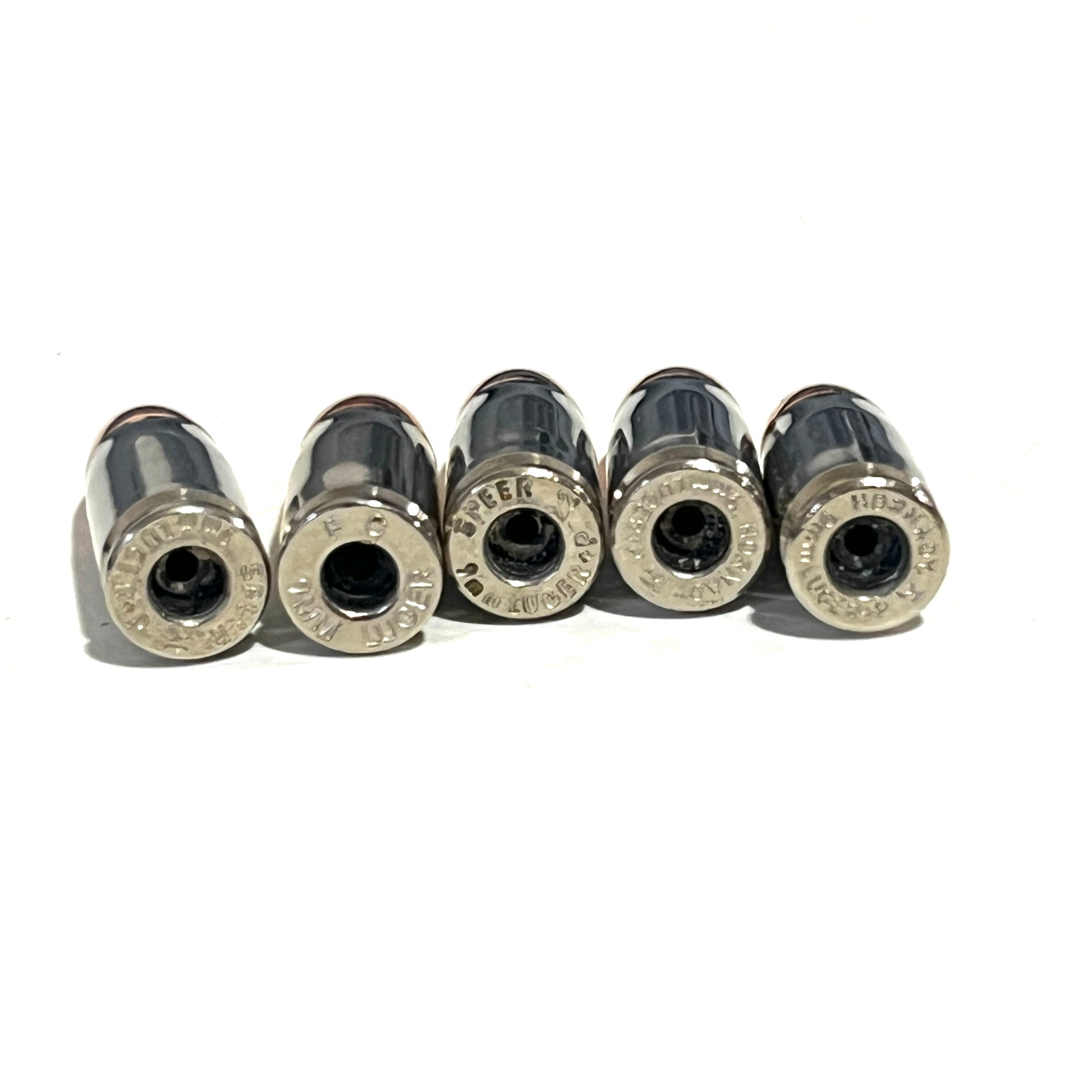 Five nickel 9mm casings lying on their sides, showing empty primer pockets and varied headstamps.