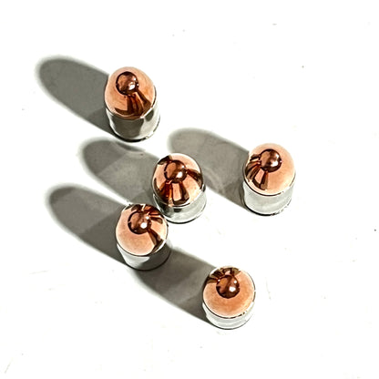 Overhead view of five nickel 9mm inert rounds with copper tips casting long diagonal shadows on white.