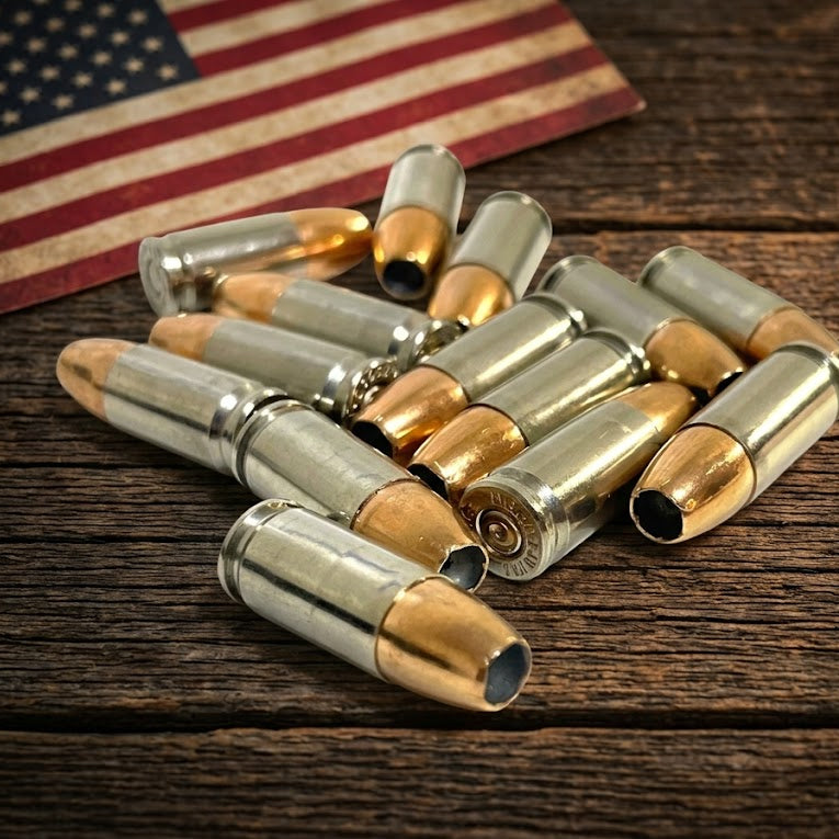  Inert 9MM Luger nickel dummy rounds arranged on a dark rustic barn wood surface with a vintage American flag in the background. Genuine once-fired casings.
