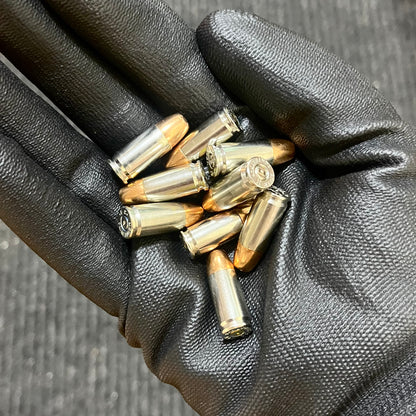 Pile of inert 9MM Luger nickel-plated once-fired dummy rounds with new jacketed hollow point (JHP) bullets. Handheld black glove. Safe for crafts, cosplay, and display.