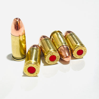 Five 9mm snap caps in once-fired polished brass with copper round-nose bullets and red primers, one standing upright