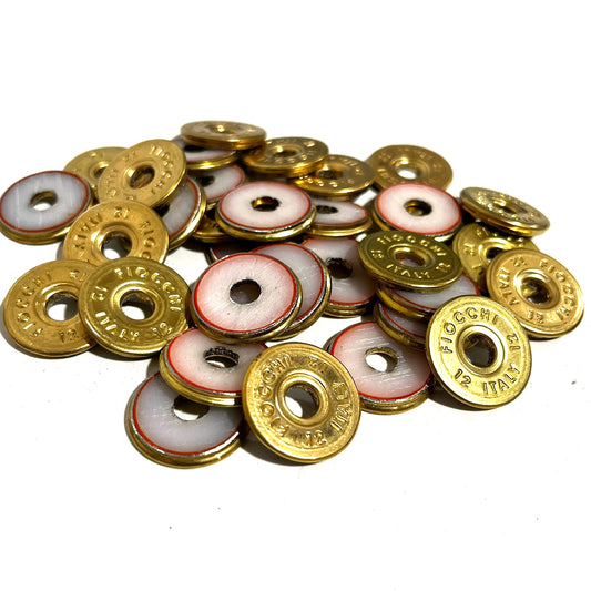 Pile of round brass 12 gauge Fiocchi Italy deprimed slices with white and red enamel-lined centers on a white background