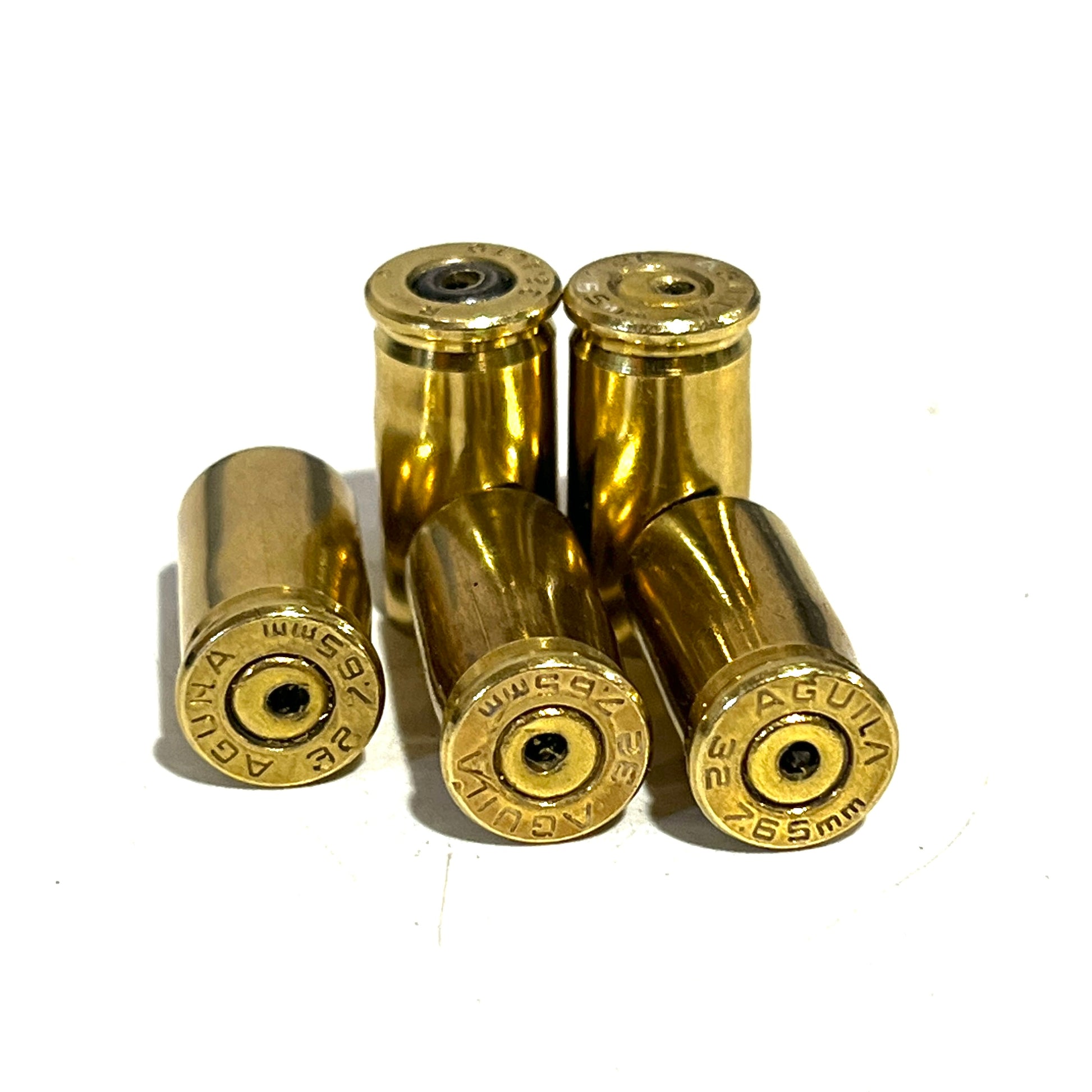 Five drilled AGUILA .32 Auto brass casings grouped on white showing headstamps and center drilled holes.