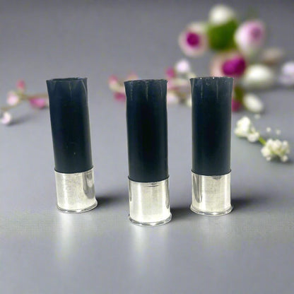 Three black shotgun shells with high brass bottoms standing among blurred pink and white flowers