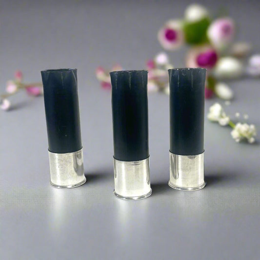 Three black shotgun shells with high brass bottoms standing among blurred pink and white flowers