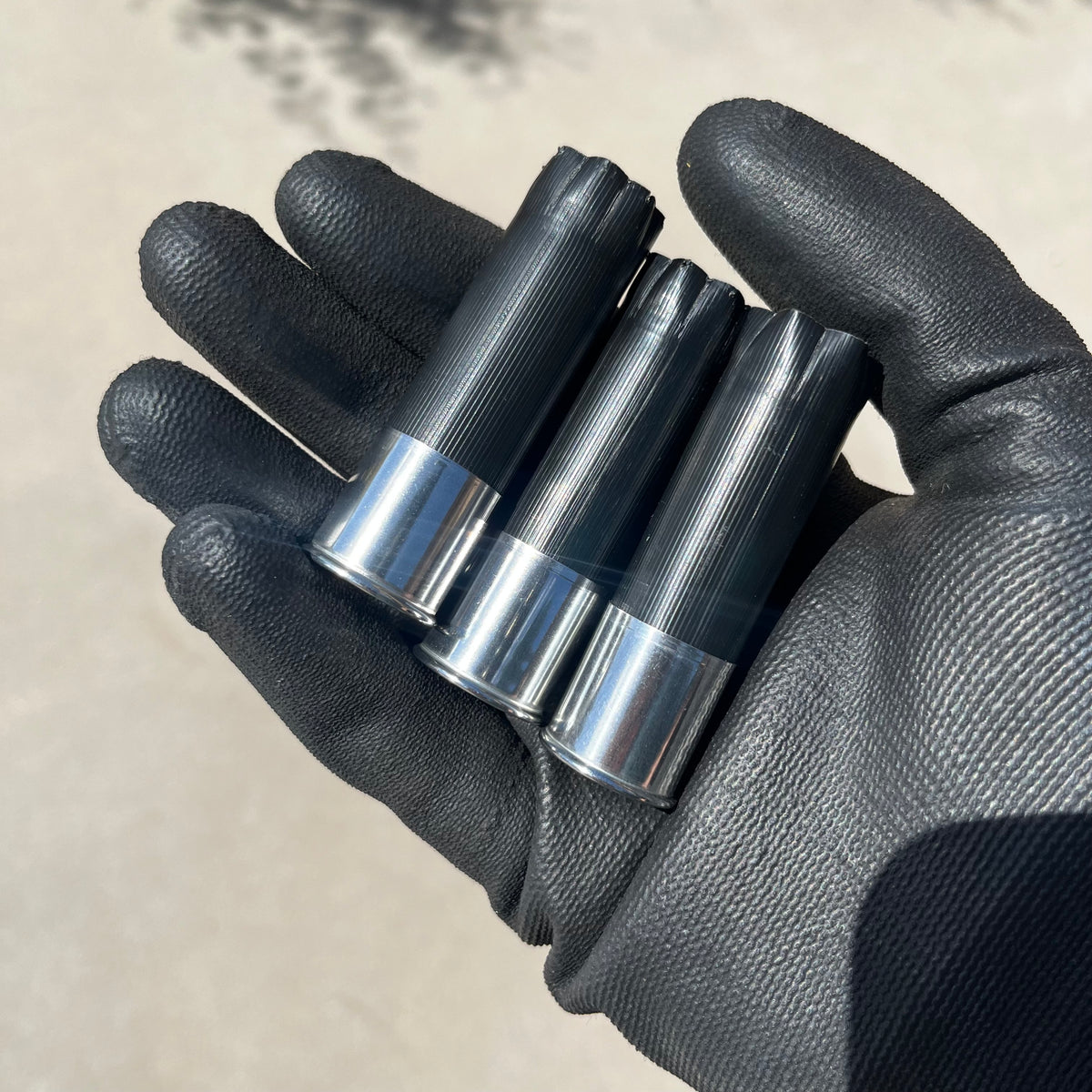 Three black shotgun shells with high brass bottoms held in a black gloved hand